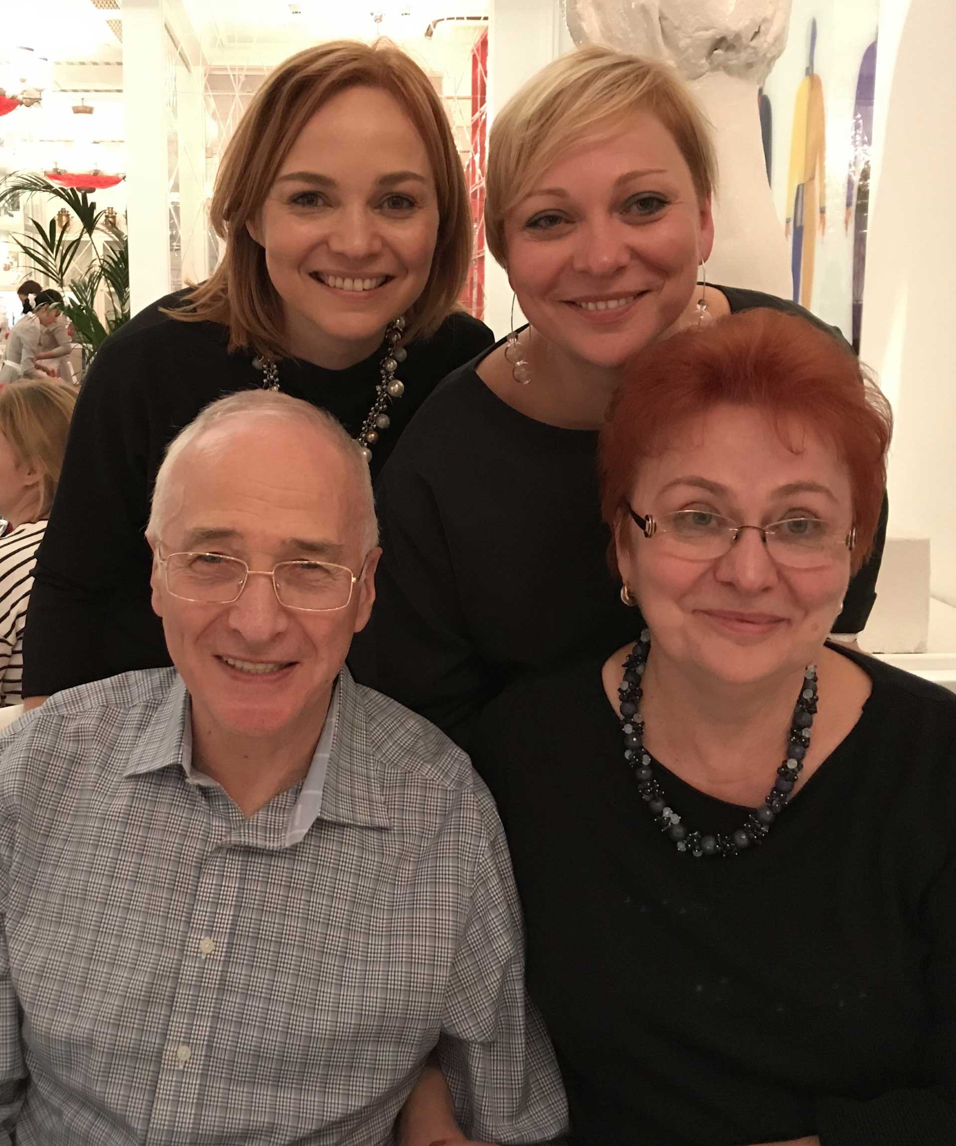 Two women standing behind an older man with glasses and an older woman with glasses