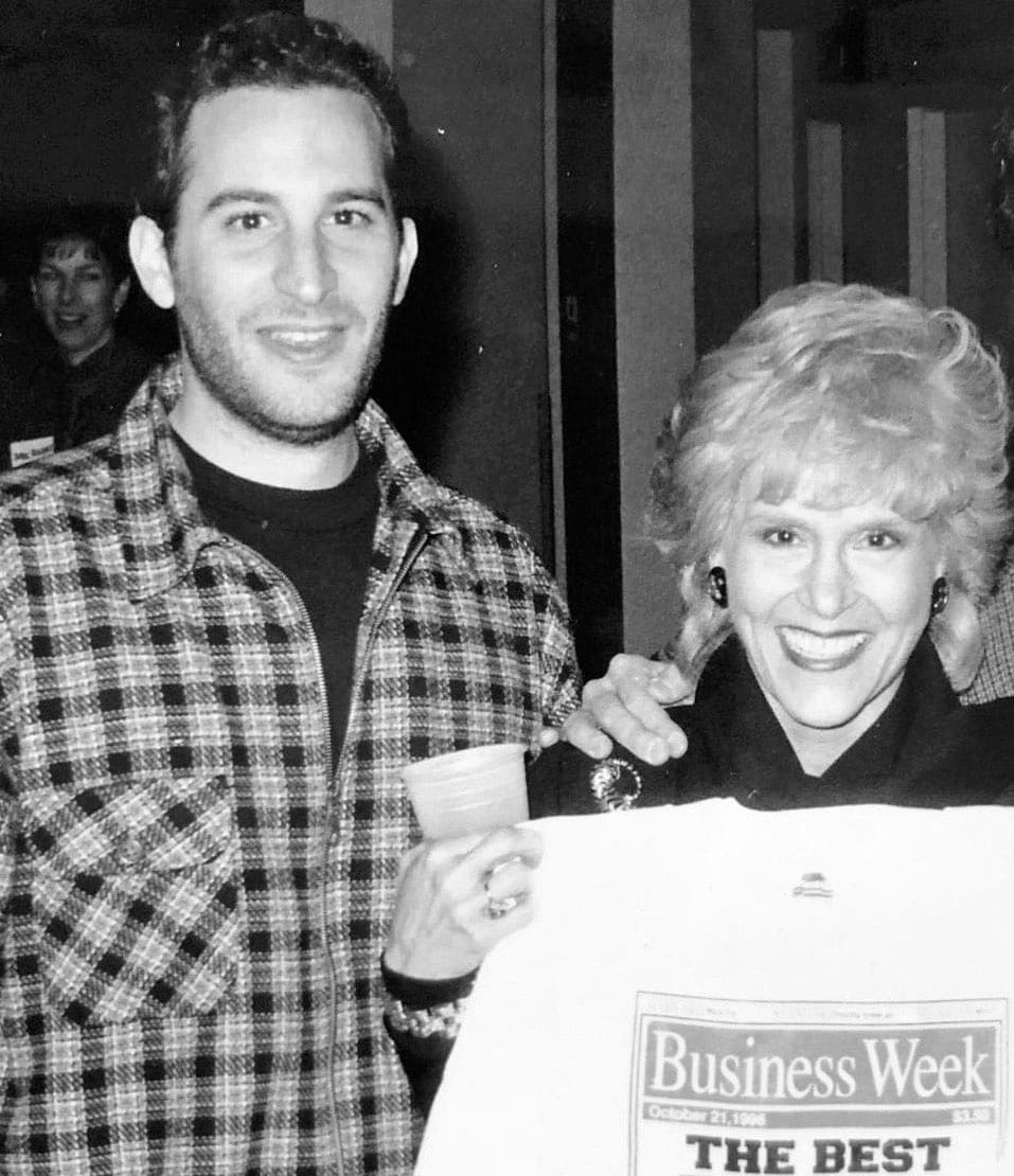 A man in a flannel jacket stands next to a woman holding a white T-shirt with the Business Week logo on it.