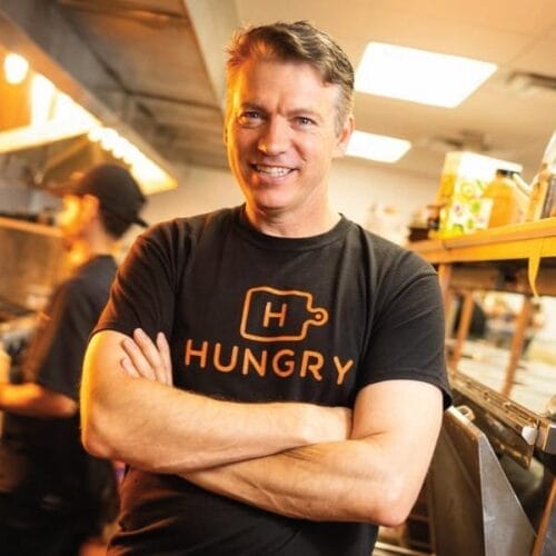 Man standing with crossed arms in a kitchen wearing a black shirt that says 