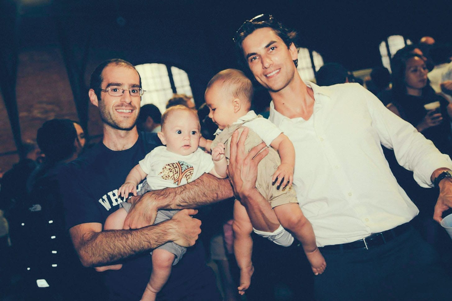 Two men pose for a photo. Each one holds a baby.