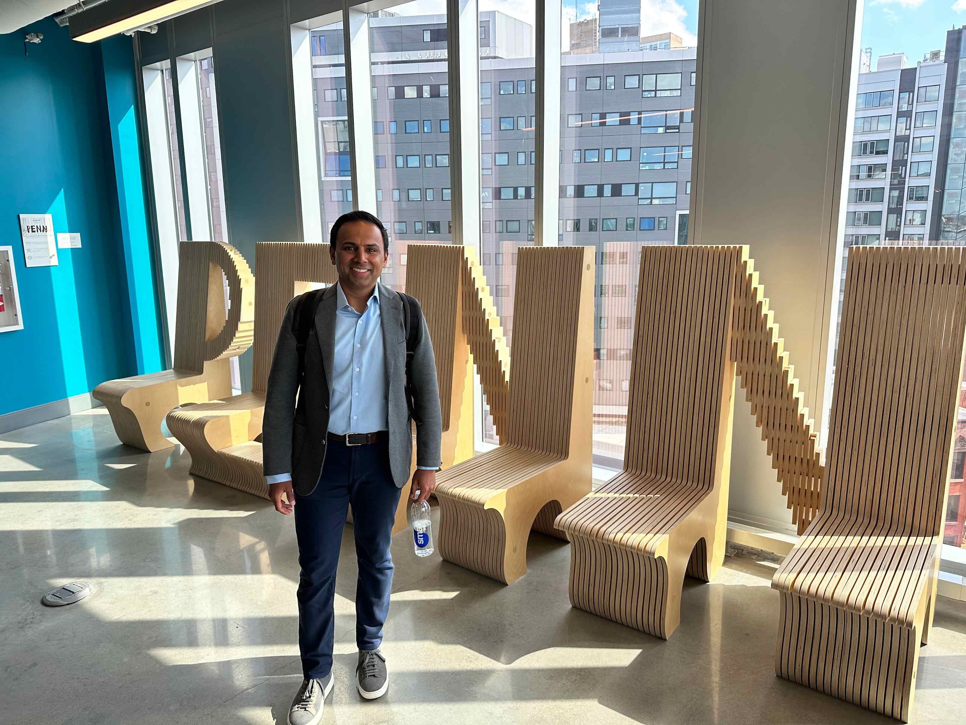 Man standing in front benches that spell out "Penn" in a room full of windows