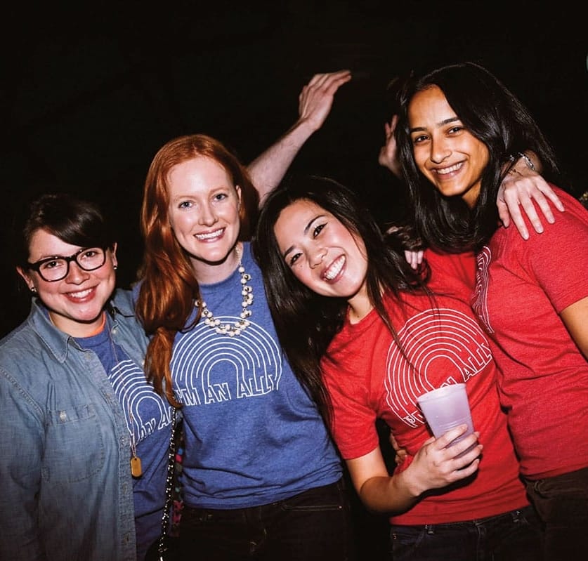 Four women in red and blue shirts that say "I'm an ally" on them.