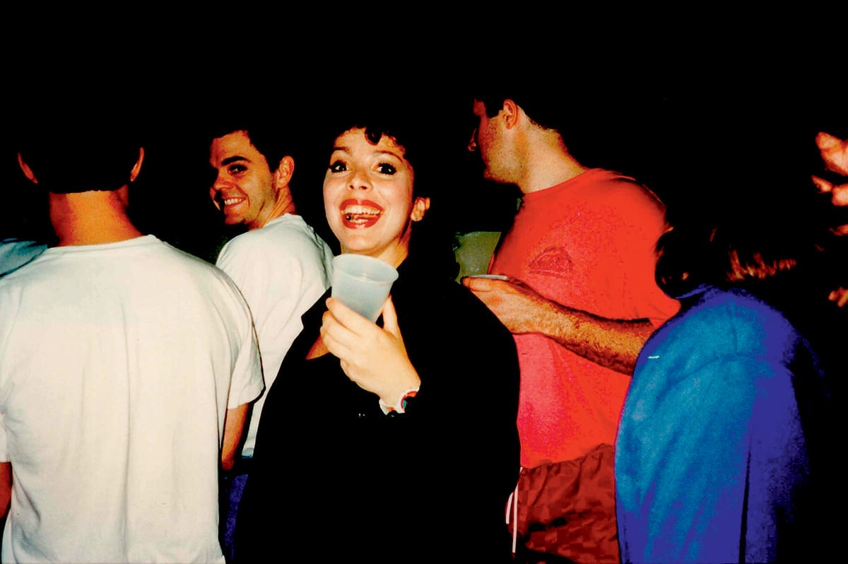 A woman among a group of people turns around and smiles for a photo.