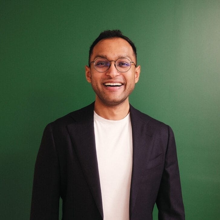 Headshot of a man smiling in front of a green background.