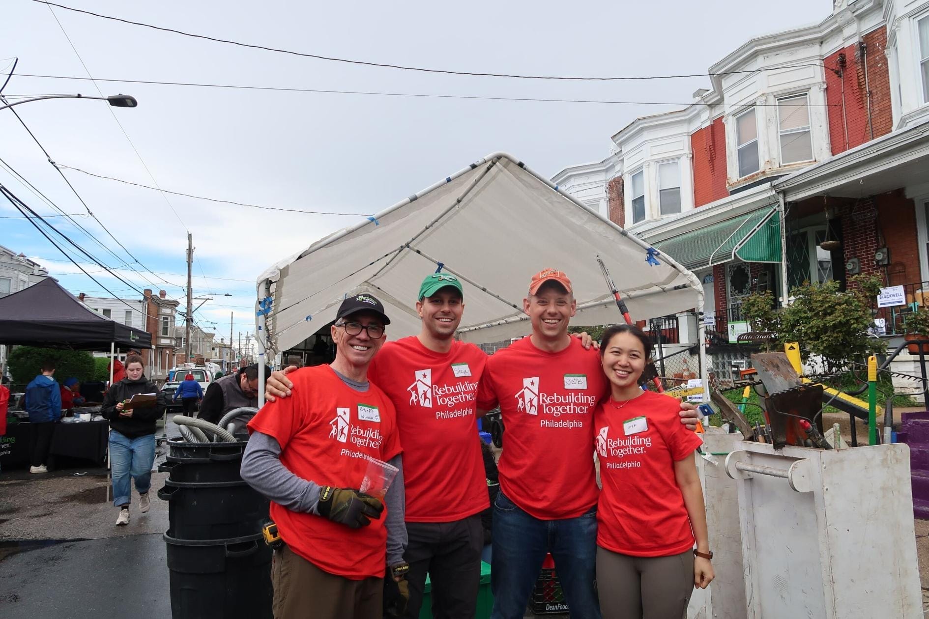 Four people wearing shirts for Rebuilding Together Philadelphia and on-site in a Philadelphia neighborhood for one of the organization's initiatives.