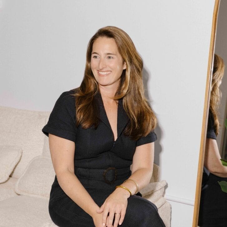 Woman sitting on a couch and smiling, looking to the side.