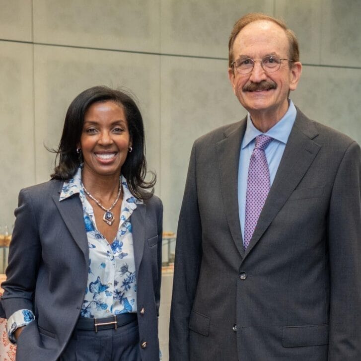 Woman in a blouse and jacket standing next to a man in a suit and tie.