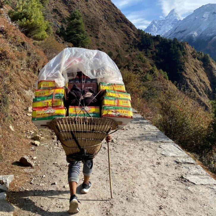 Person hiking up a mountain with a stick while carrying a large piece of luggage