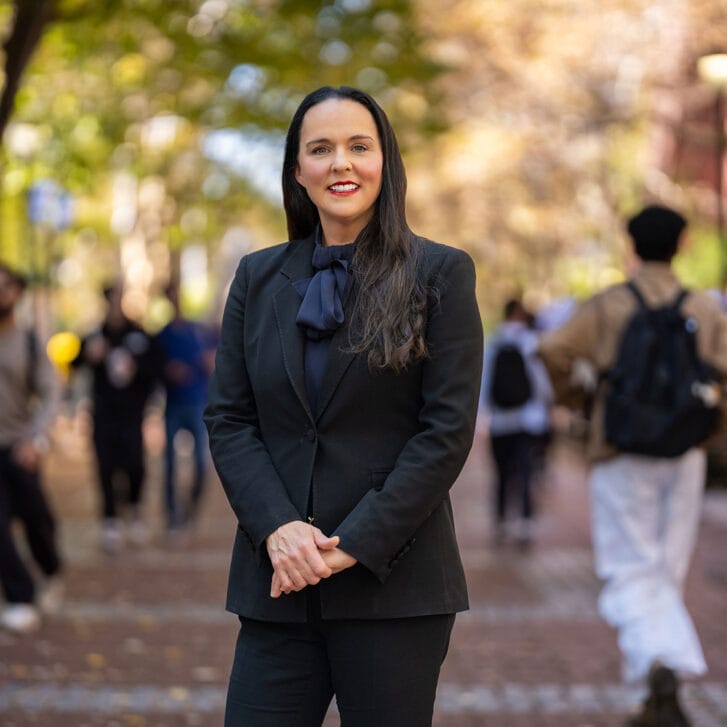 Woman standing outside on a busy college campus as students with backpacks walk around her