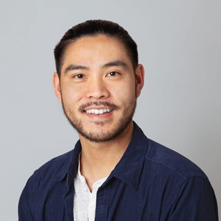 Headshot of a man smiling and wearing a navy jacket with a white shirt underneath.