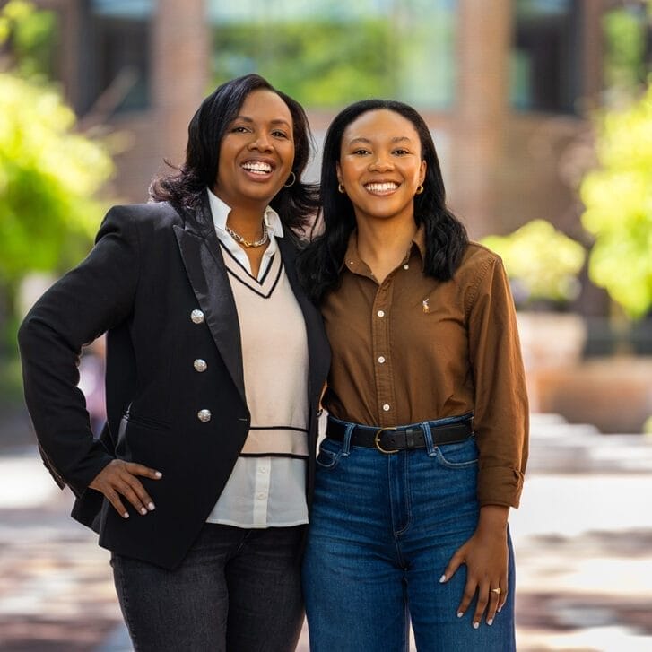 Two women standing together, embracing, outside in front of a building and trees