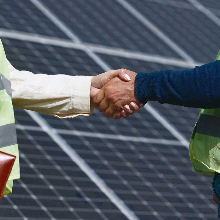 Close-up of a handshake between two people as they stand in front of solar panels