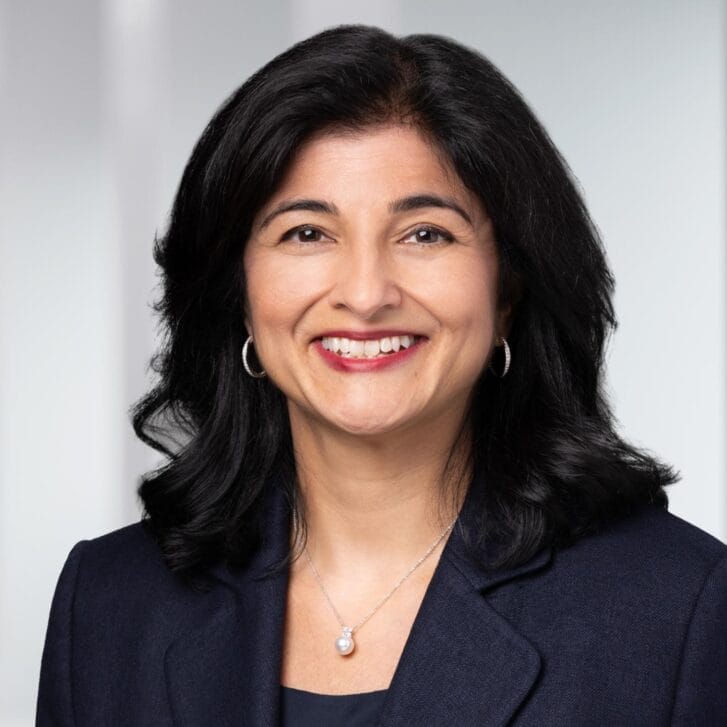 Woman with black hair in a black suit jacket and silver jewelry.