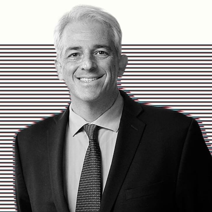 Photo portrait of a man in a suit and tie with his hands clasped behind his back.