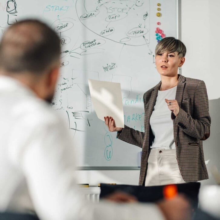 Woman speaking in front of a whiteboard and in front of colleagues or board members