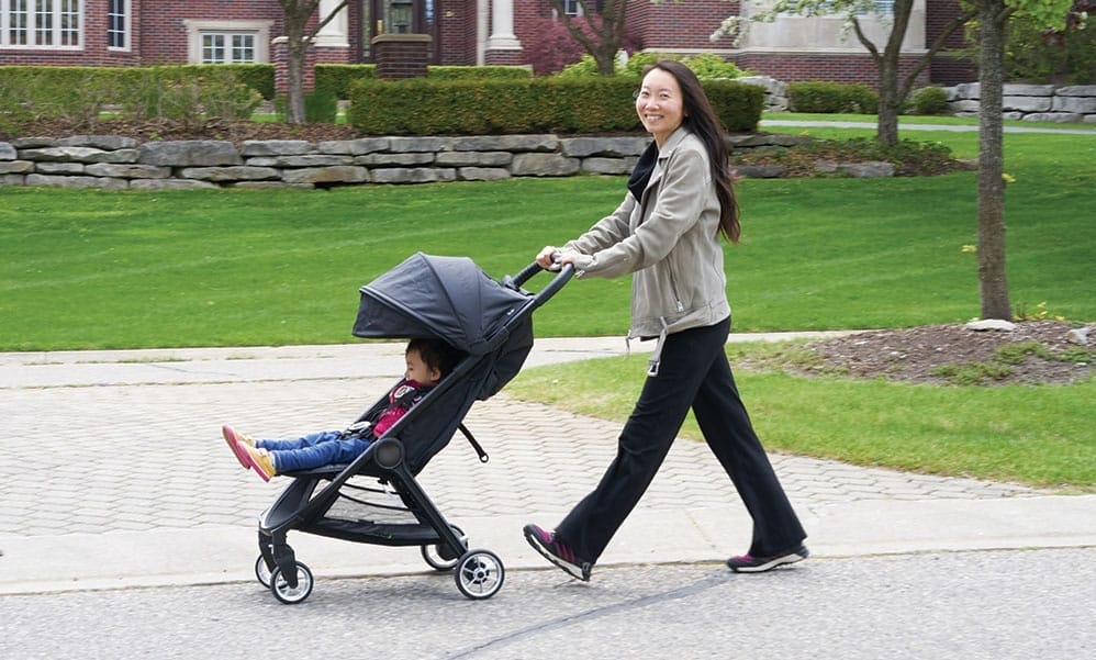 A woman pushes a baby in a stroller outside.