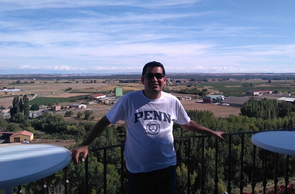 A man stands outside on a balcony in a Penn t-shirt.