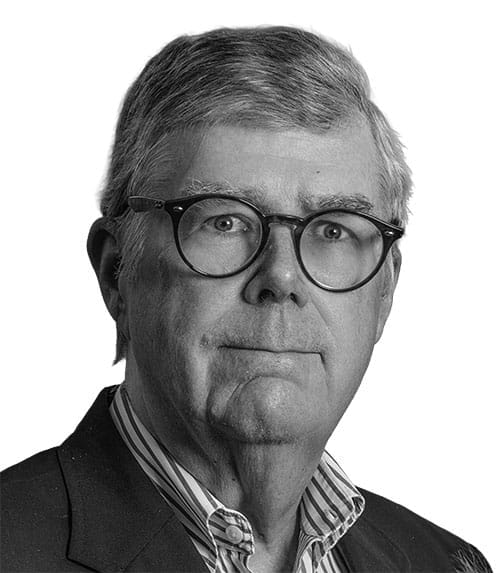 Headshot of a man in a suit jacket, striped button-down shirt, and black-rimmed glasses.