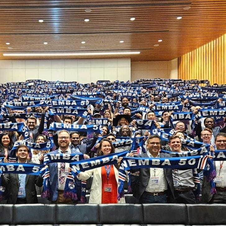 Hundreds of Wharton students stand in auditorium rows holding up blue scarves with the words 