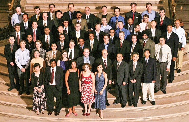 Dozens of people in business attire pose together on a set of tan steps.
