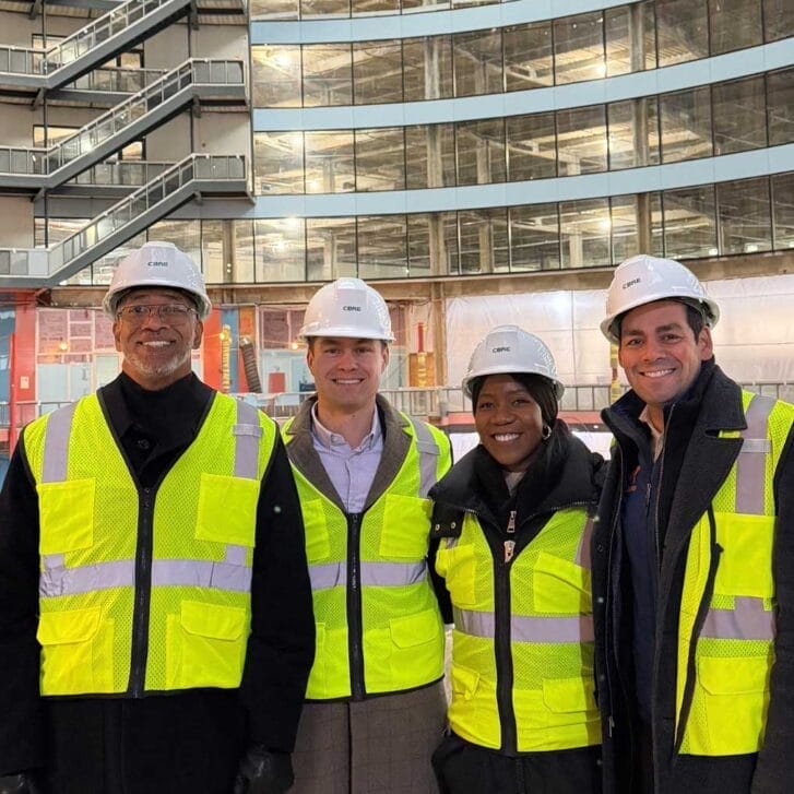Group of people in yellow vest and hardhats standing in front of a construction site