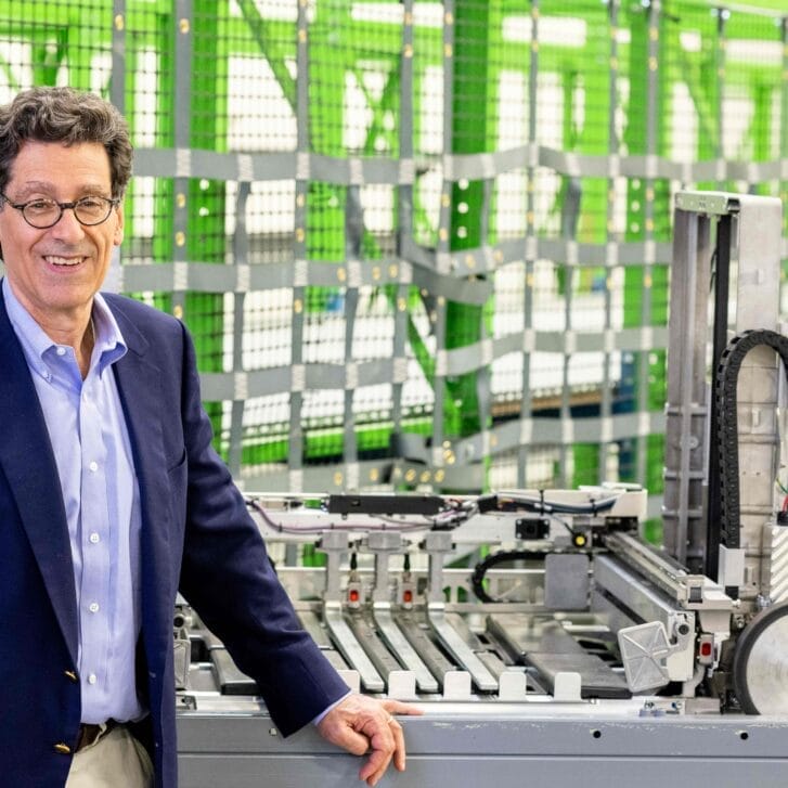 Man smiles and stands in front of robotic wheels and frame