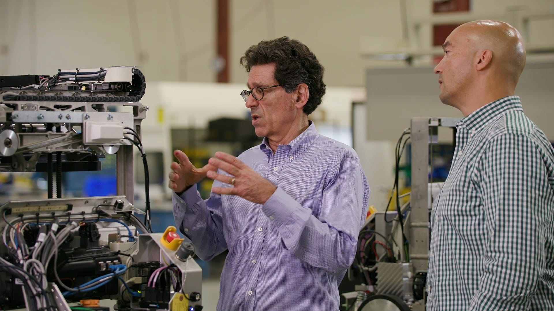 Man gestures toward robot as another man listens and stands nearby